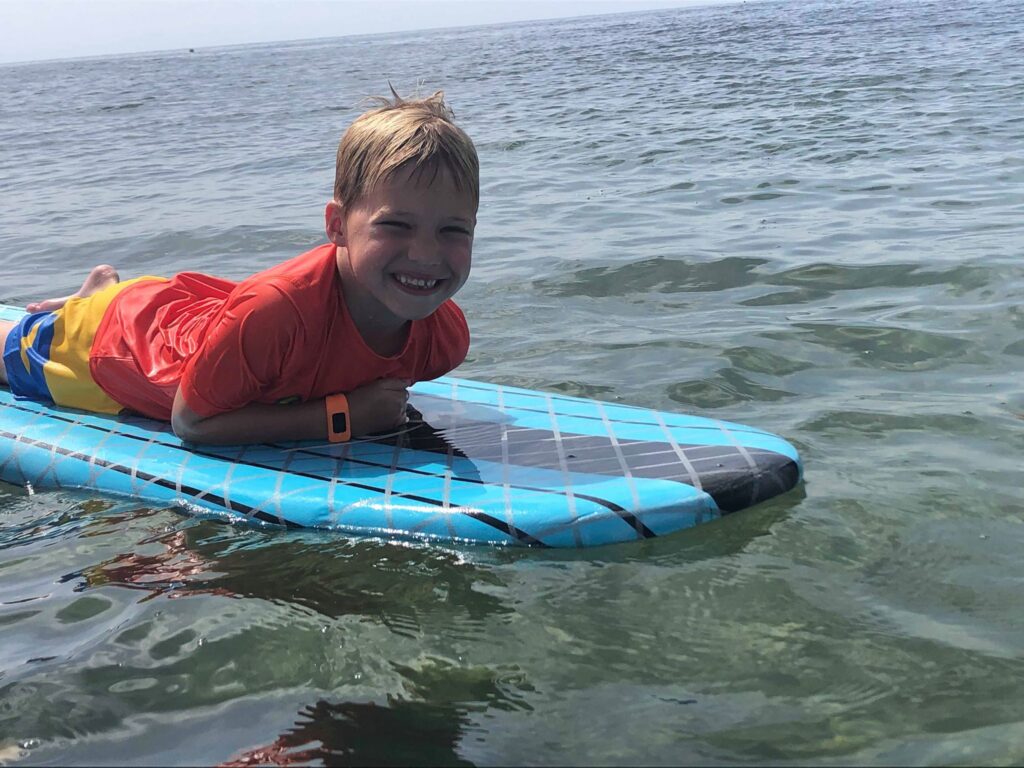 Boy grinning while lying on a paddleboard during a lesson in calm shallow water