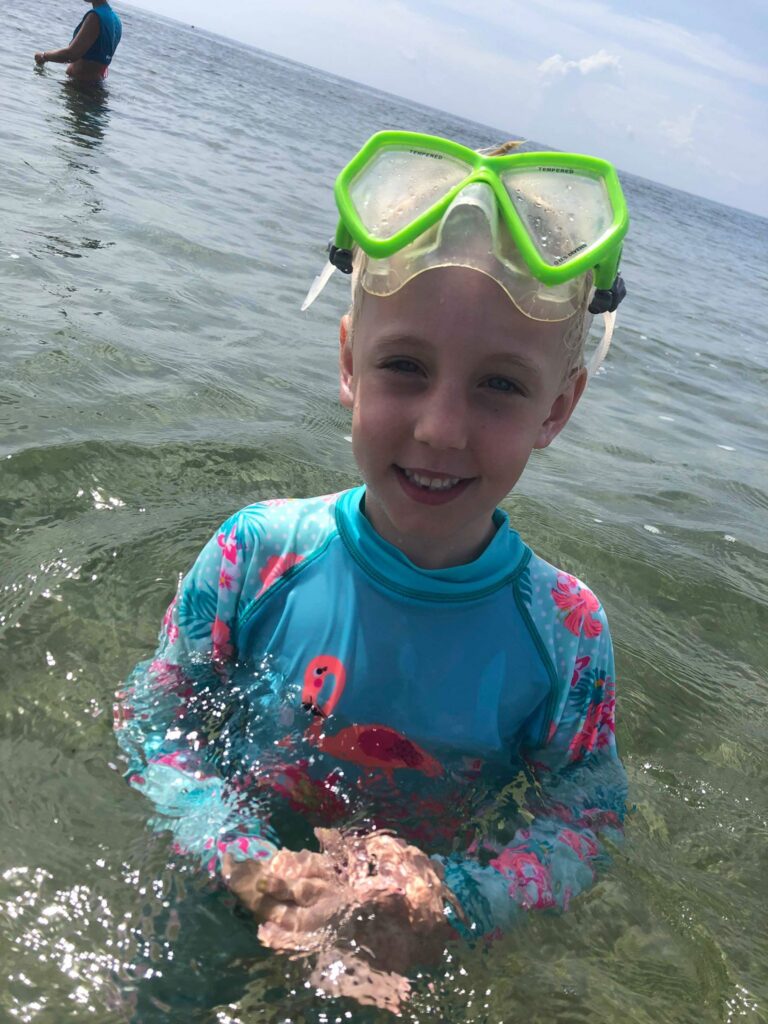 Girl in a snorkel mask holding a shell she found in shallow water
