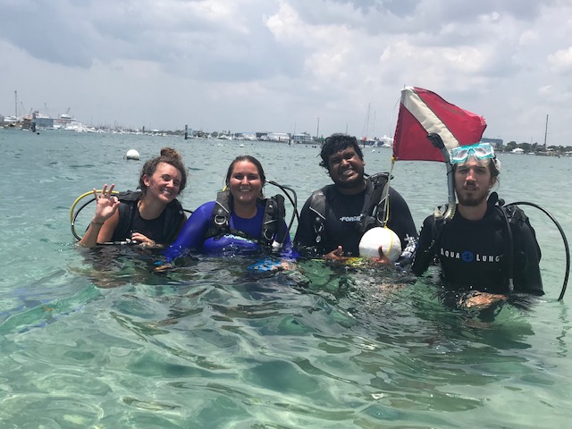 Four scuba divers in shallow water with a dive flag after an open water dive in Florida