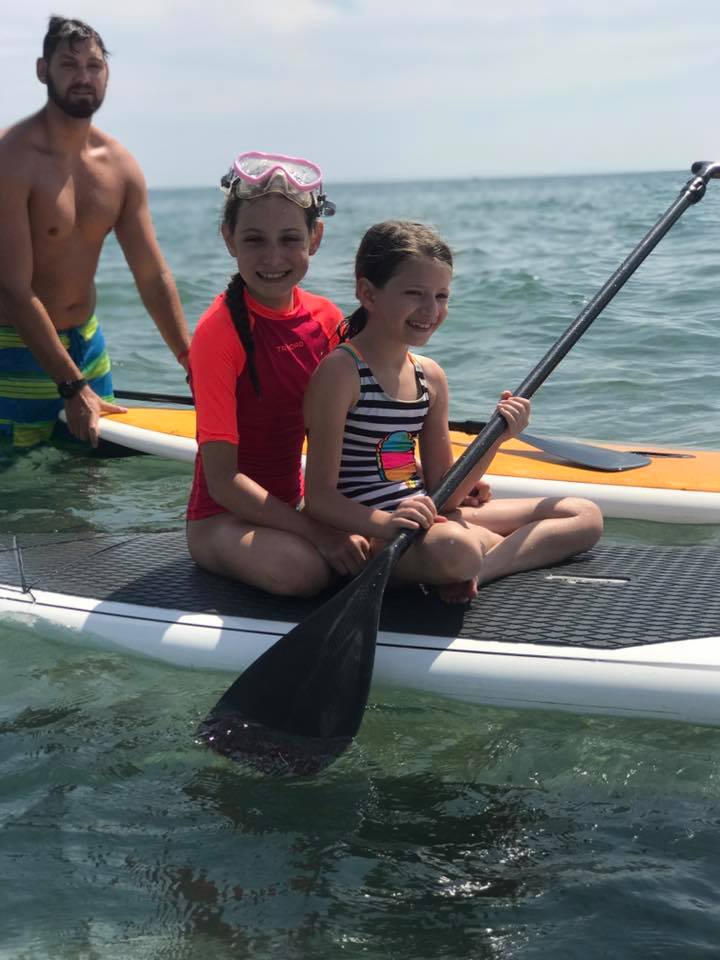 Two campers paddleboarding on calm ocean with an instructor