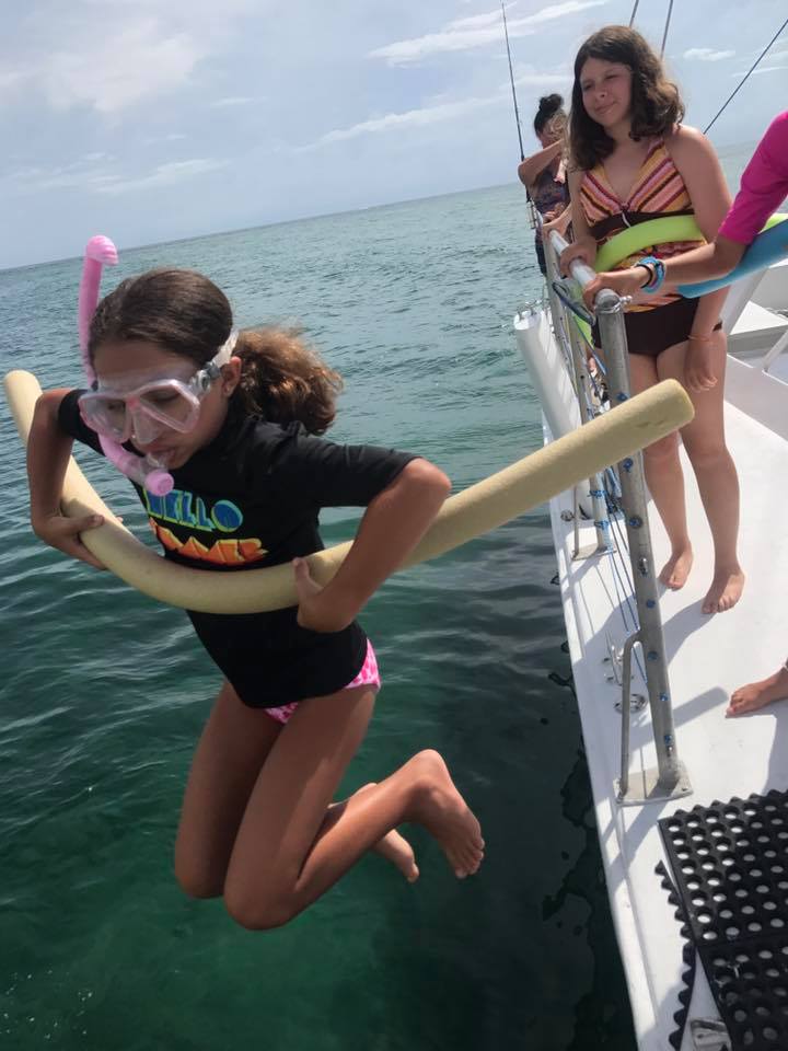 Camper in snorkel gear jumping off the boat with a pool noodle